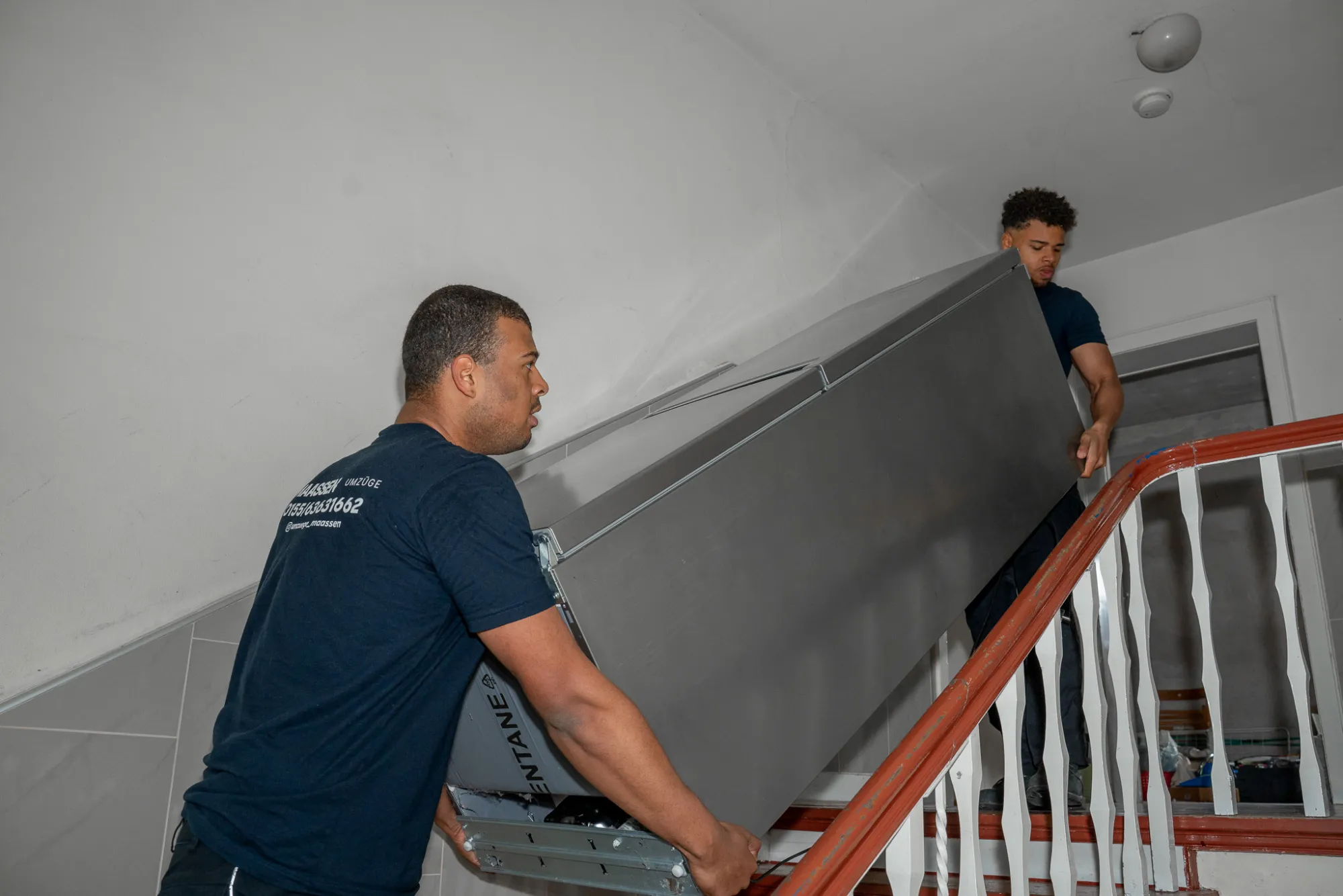Firmenumzug Krefeld – Umzugshelfer von Maassen Umzüge tragen einen Kühlschrank die Treppe hoch
